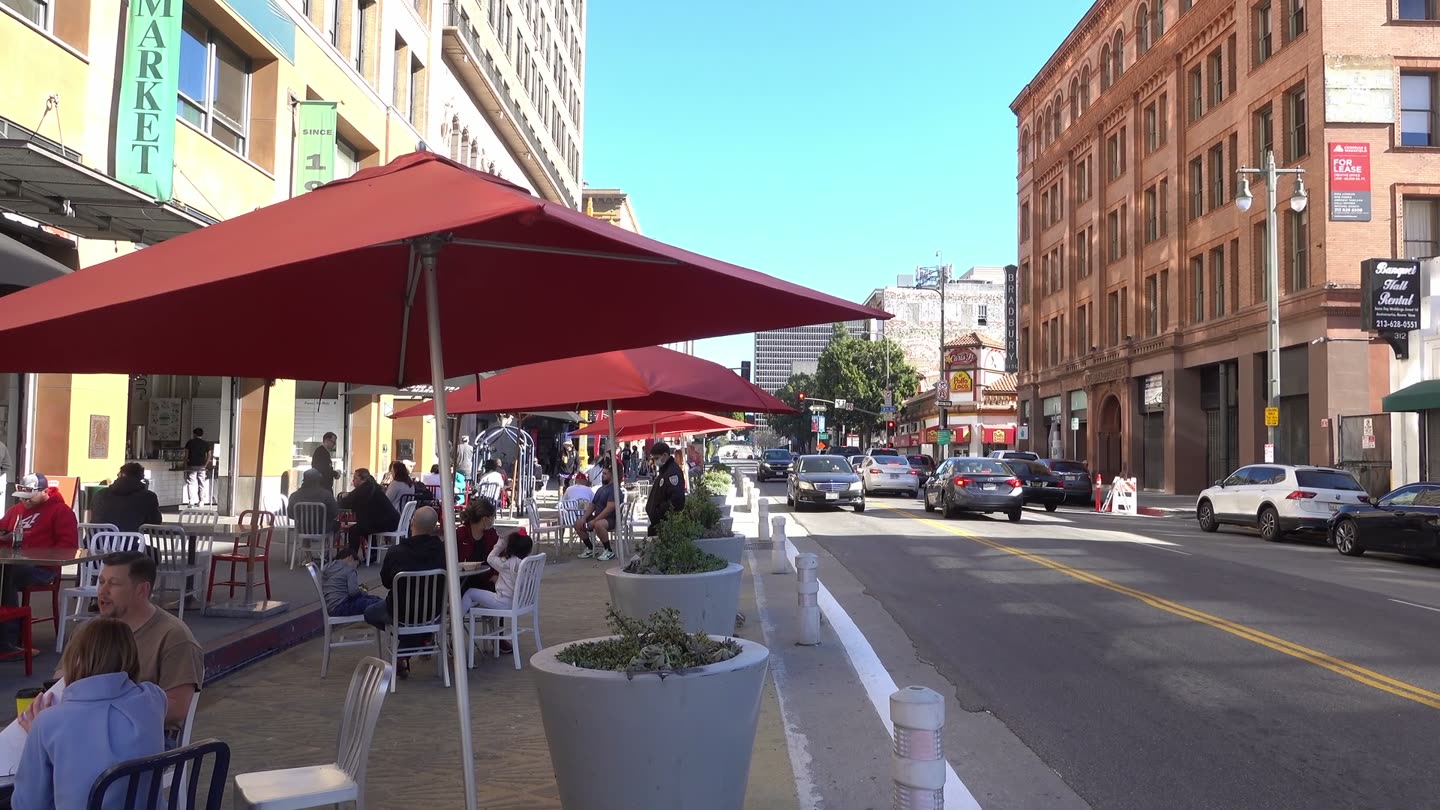 Outdoor tables under red umbrellas on the Hill Street side of Grand Central Market