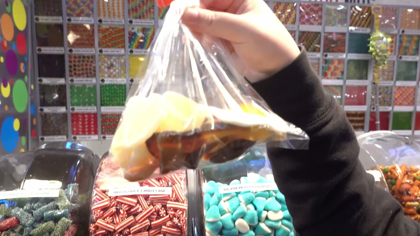 Holding up a clear bag of candy in front of rows of candy bins at La Huerta