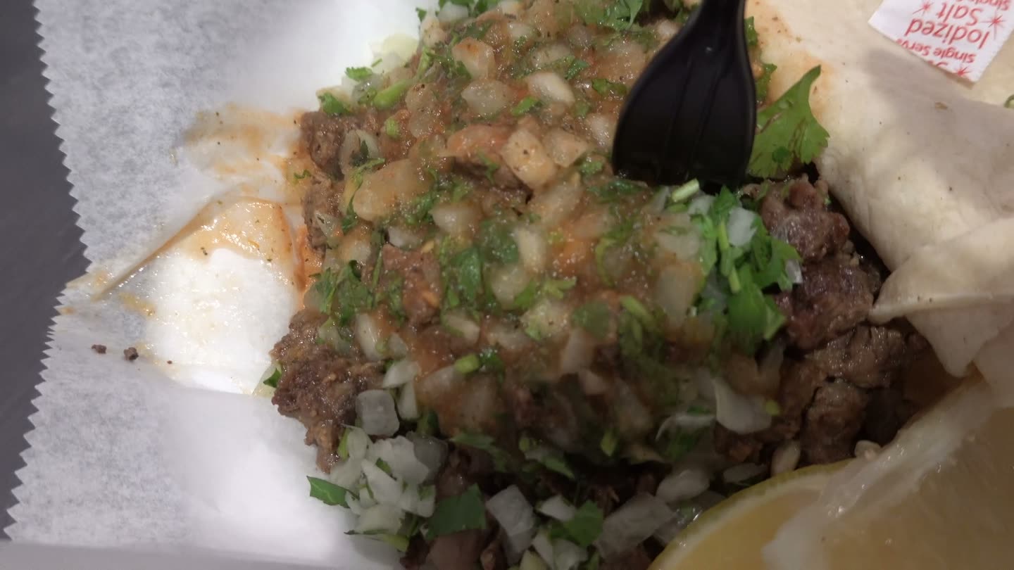 An overstuffed carne asada taco with onions, cilantro, and lime on wax paper