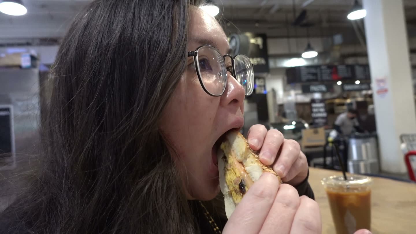 Lisa taking a big bite of a lox and egg bagel sandwich at the market