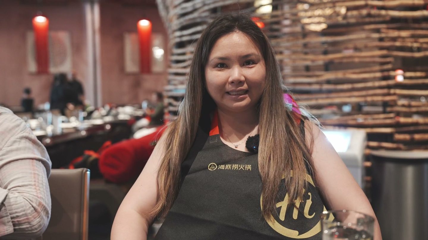 Lisa smiling in a black Haidilao apron at the table