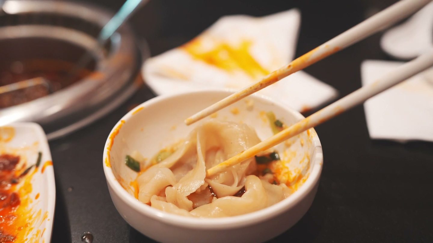 A bowl of wide hand-pulled noodles in broth with chili and scallions