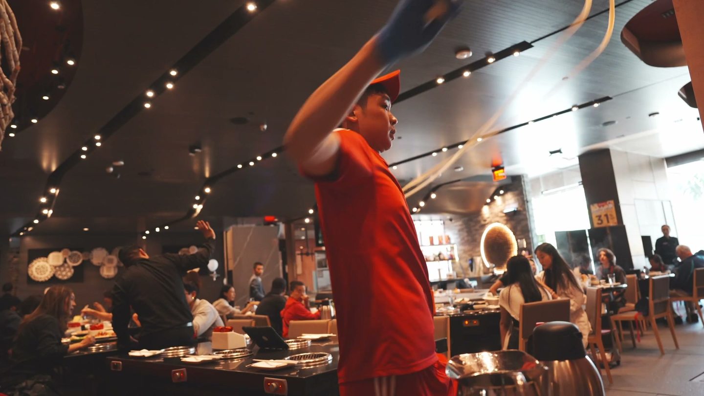The noodle server raising a ribbon of noodle dough overhead in the middle of the dining room