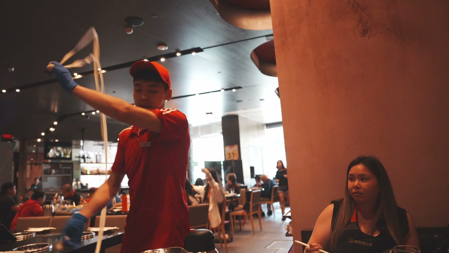 A Haidilao server spinning noodle dough beside our table while Lisa watches