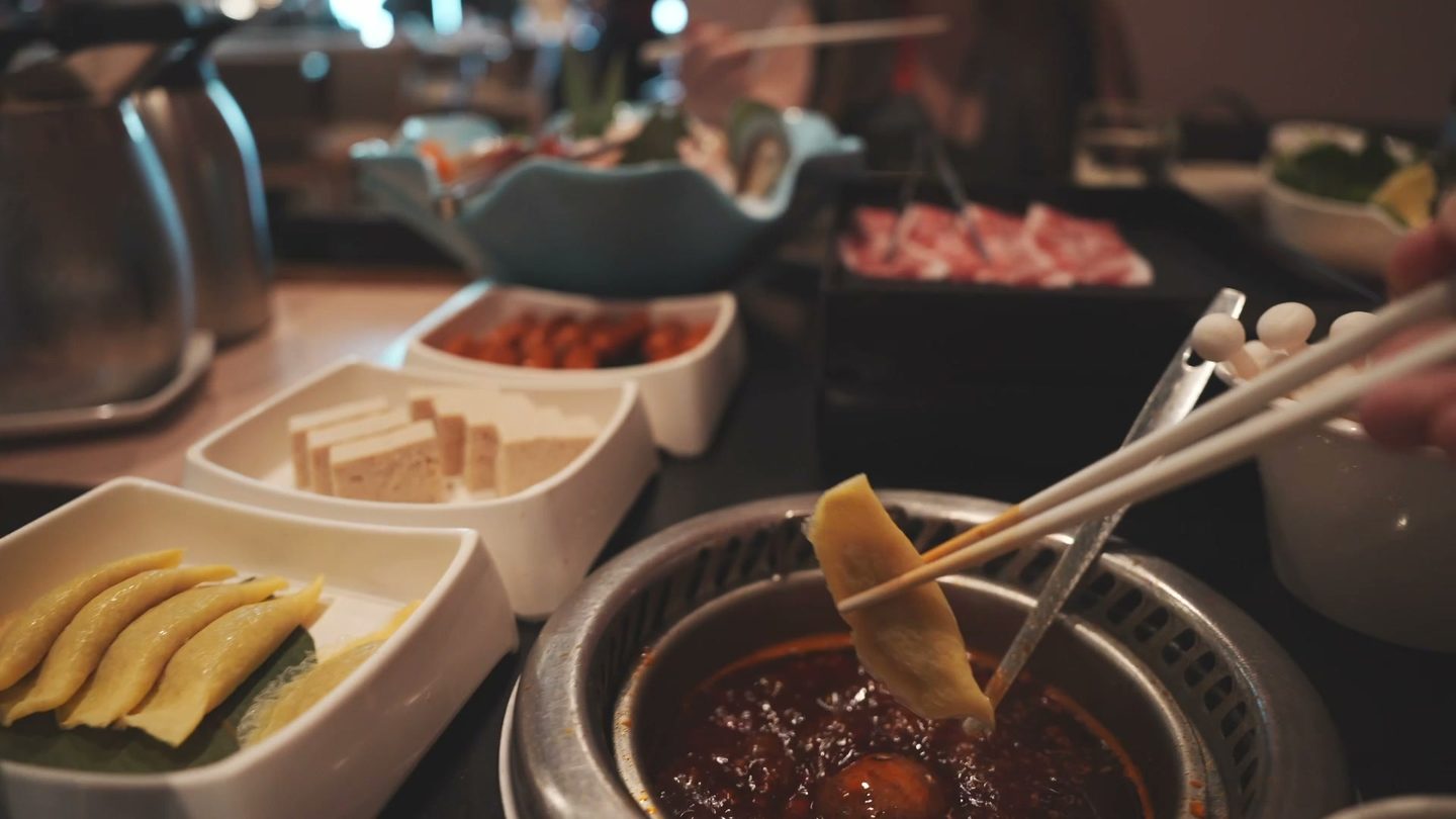Chopsticks lifting a yellow egg dumpling out of the spicy hot pot