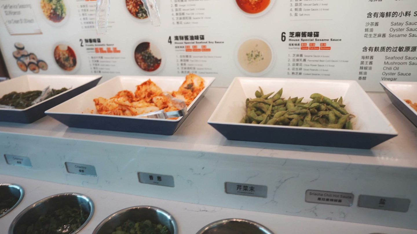 Haidilao sauce bar with kimchi, edamame, and rows of sauces under a menu of sauce recipes