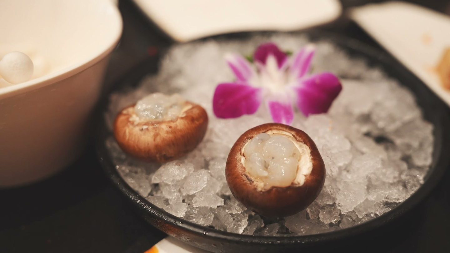 Two shiitake mushroom caps stuffed with shrimp paste on a bed of ice with an orchid