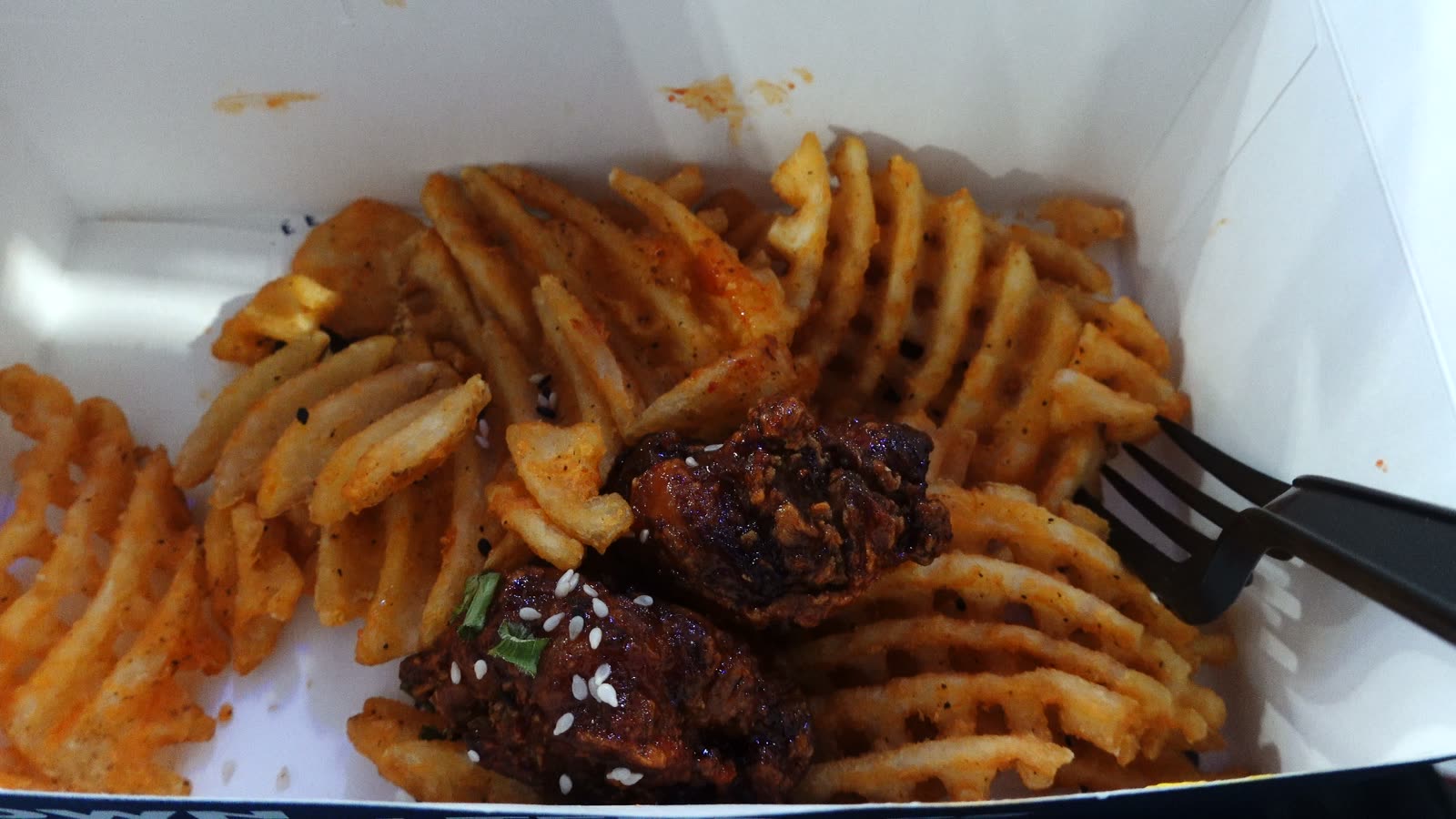 Korean fried chicken pieces over waffle fries in a box at Intuit Dome
