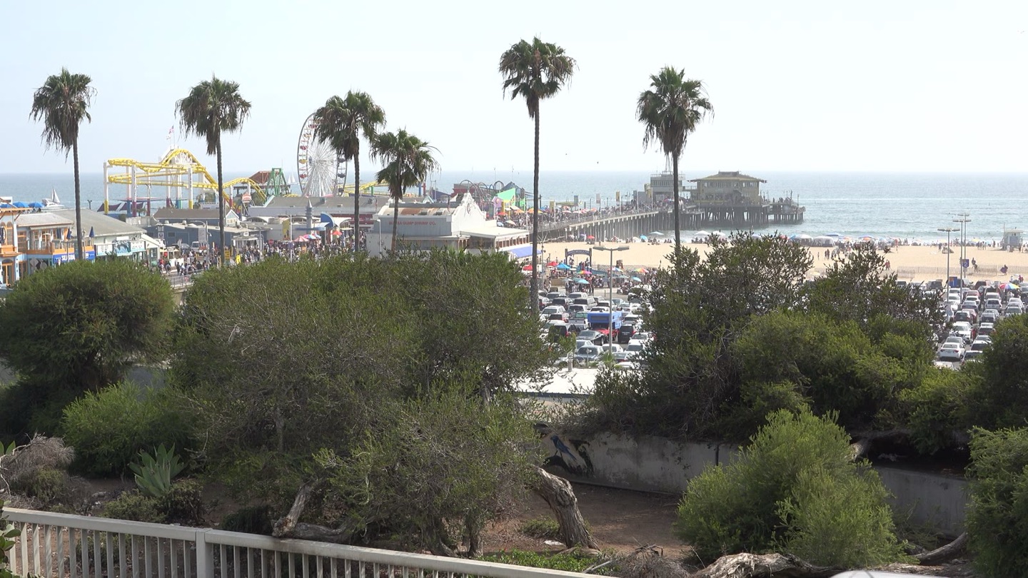 The Santa Monica Pier and its Ferris wheel seen from the bluff, with crowds on the beach below