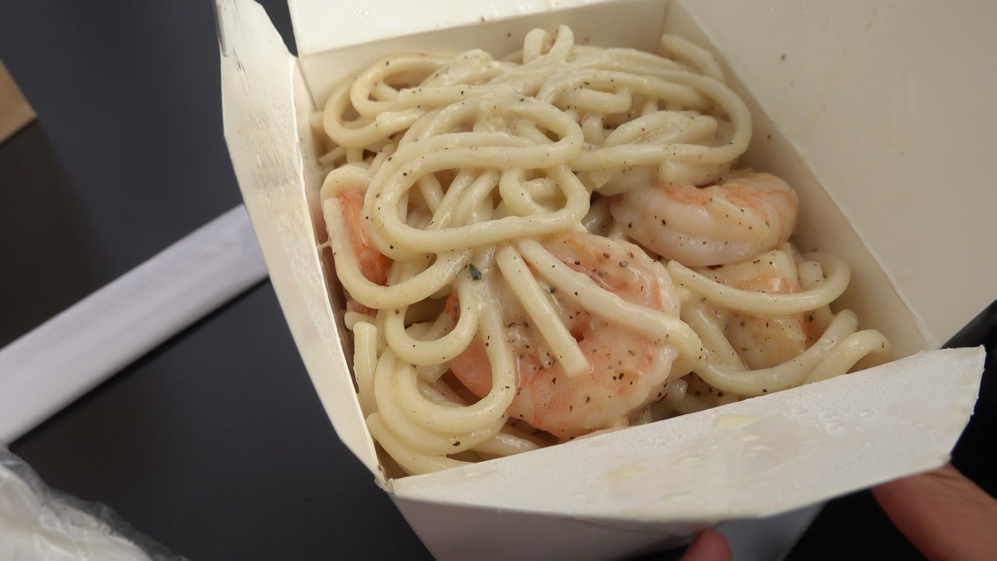 A takeout box of udon cacio e pepe with shrimp