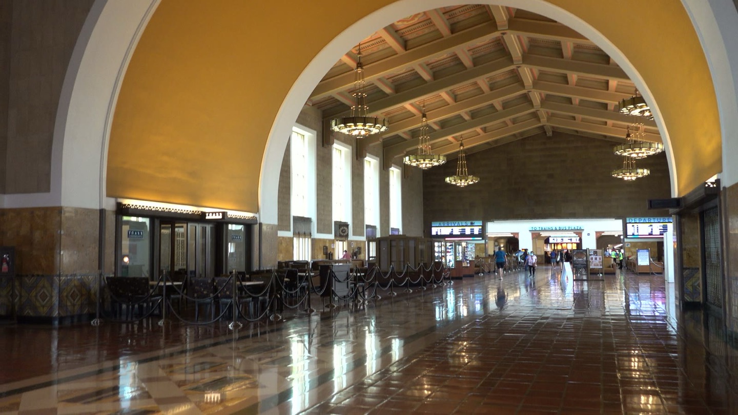 The main waiting room at Los Angeles Union Station, with tall arched windows, chandeliers, and a polished tile floor