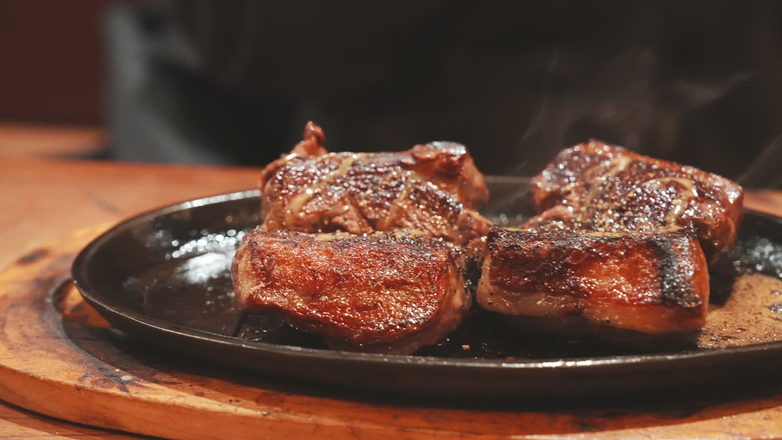 Two seared New Zealand lamb rumps cut into pieces on a sizzling plate at Angus Steak House